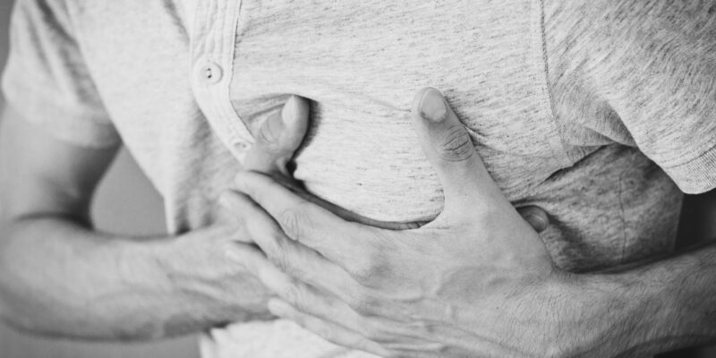 Man in poloshirt houdt zijn hand op de linkerkant van zijn borst, zwart-witfoto over hartkloppingen