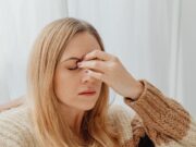 Vrouw in een warme trui zit binnen met haar hand tegen haar hoofd door hoofdpijn of een migraineaanval