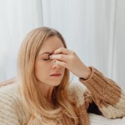 Vrouw in een warme trui zit binnen met haar hand tegen haar hoofd door hoofdpijn of een migraineaanval