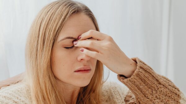 Vrouw in een warme trui zit binnen met haar hand tegen haar hoofd door hoofdpijn of een migraineaanval