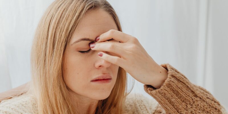 Vrouw in een warme trui zit binnen met haar hand tegen haar hoofd door hoofdpijn of een migraineaanval