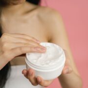 Vrouw neemt witte crème uit een open pot om op een geïrriteerde huid aan te brengen