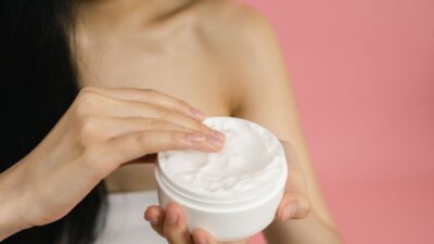 Vrouw neemt witte crème uit een open pot om op een geïrriteerde huid aan te brengen