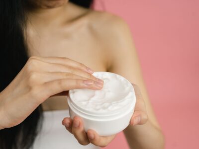 Vrouw neemt witte crème uit een open pot om op een geïrriteerde huid aan te brengen