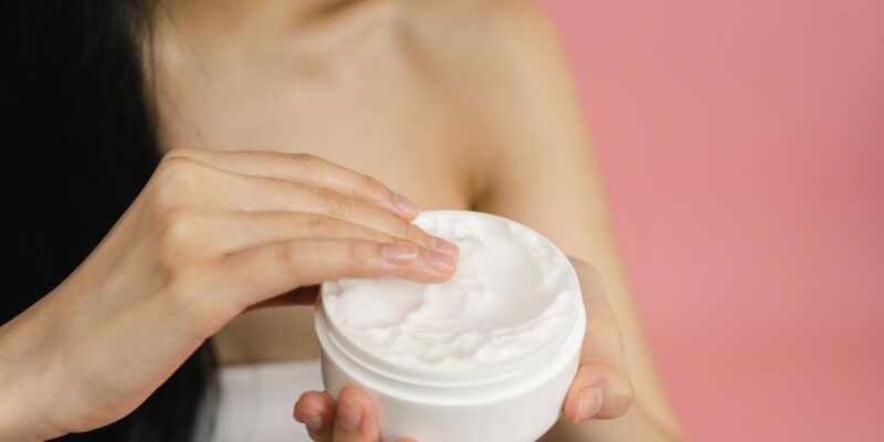 Vrouw neemt witte crème uit een open pot om op een geïrriteerde huid aan te brengen